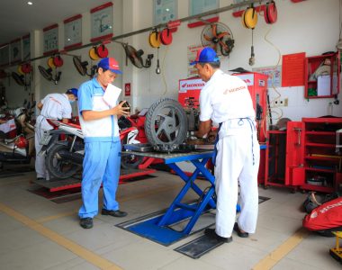 Mechanics wearing uniforms work on motorcycles inside a Honda service center.