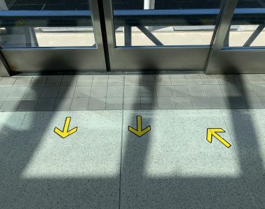 A contemporary airport hallway with yellow arrows guiding directions on the tiled floor.