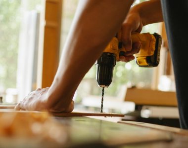 Close-up of a person using a power drill on wood indoors during daytime.